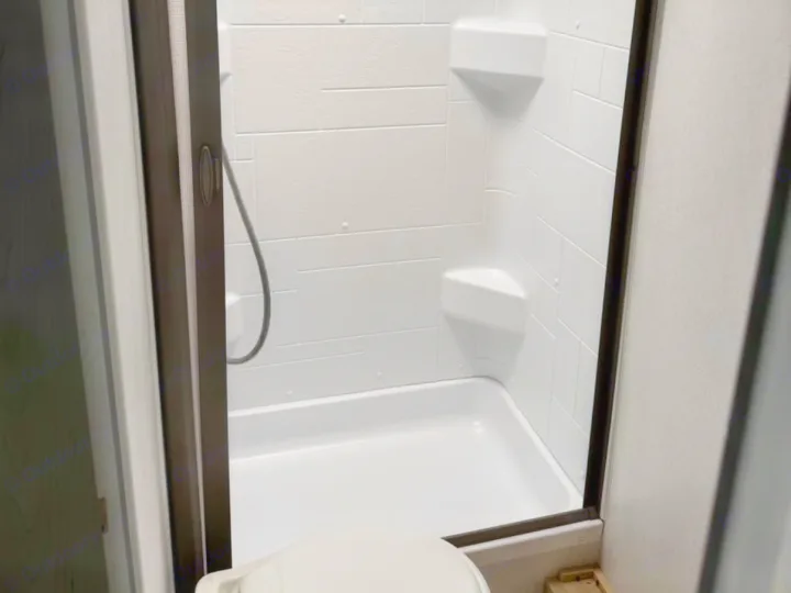 A clear view inside an RV rental bathroom with a compact white shower, built-in shelves, and toilet.. Forest River Wildwood FSX 2023