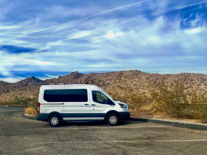 rv rental van parked in a desert landscape with rocky hills under a vibrant blue sky with visible contrails.. Ford Transit 2018