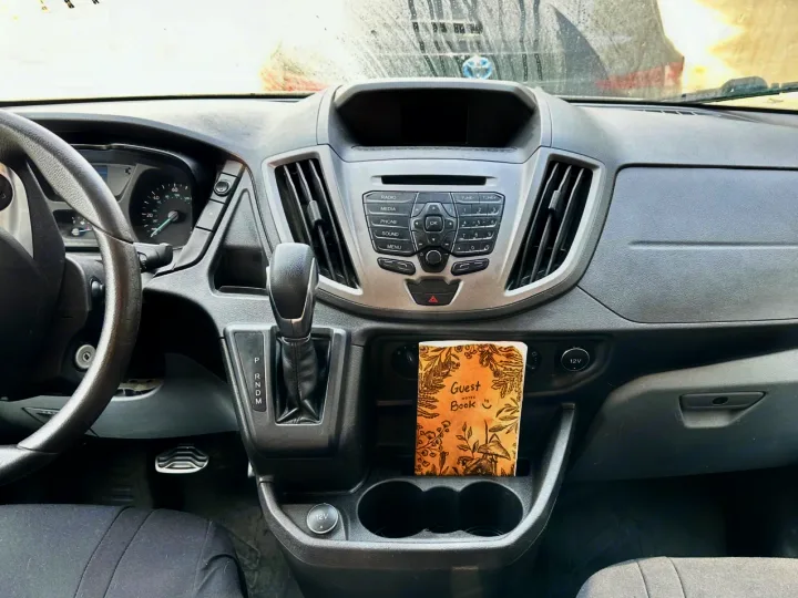 RV rental van dashboard showing steering, gear shift, radio, and a guest book in the central cup holder area.. Ford Transit 2018