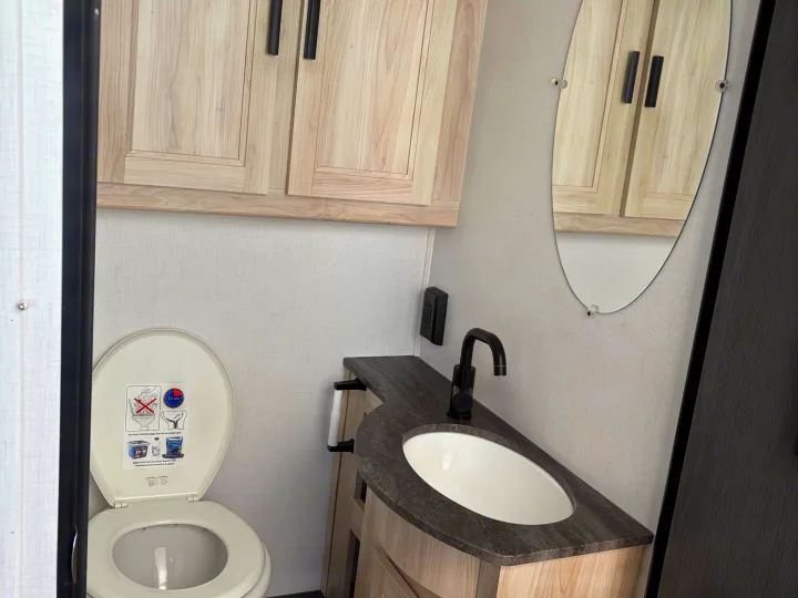 RV rental compact bathroom featuring a toilet with instructions, modern sink, black faucet, and light wood cabinets.. Forest River Sunseeker LE 2024