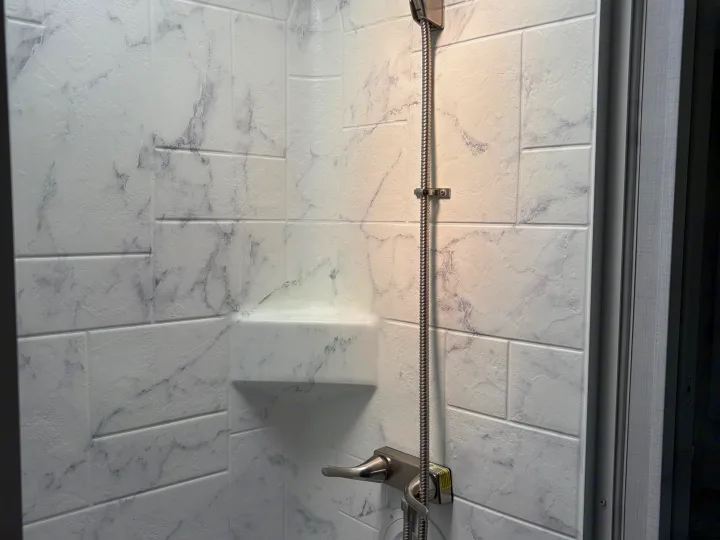 Compact, modern marble-look shower interior with a flexible showerhead and corner shelf, perfect for an RV rental.. Forest River Sunseeker LE 2024