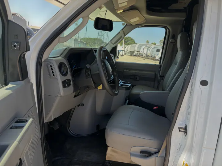 Driver's view inside a white RV rental van, featuring the steering wheel, dashboard, and front seats. RVs are visible outside.. Forest River Sunseeker LE 2024