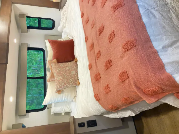 Cozy RV rental bedroom with blush decor, fluffy pillows, and forest views from the windows.. Alliance RV Avenue 2026