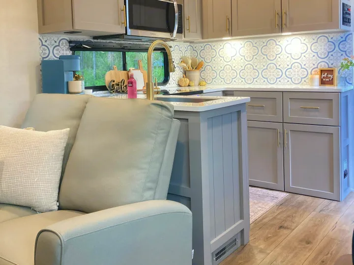Modern RV rental kitchen featuring stylish gray cabinets, a blue backsplash, and a comfy sofa for a cozy travel experience.. Alliance RV Avenue 2026