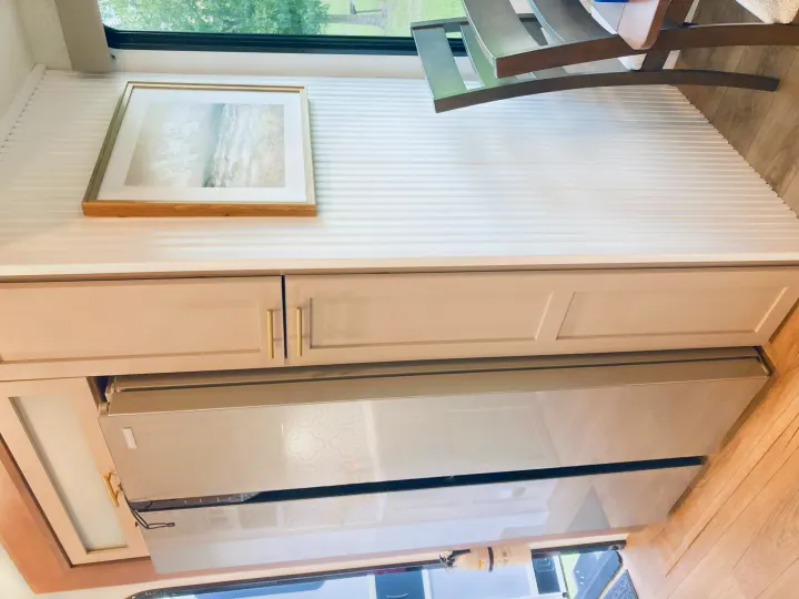 Modern RV rental interior featuring a compact kitchen with light cabinetry, sleek refrigerator, ribbed wall paneling, and wood floors.. Alliance RV Avenue 2026