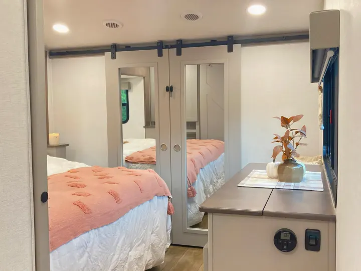 Modern RV rental bedroom boasts mirrored sliding doors, a plush bed with pink accents, and smart controls.. Alliance RV Avenue 2026