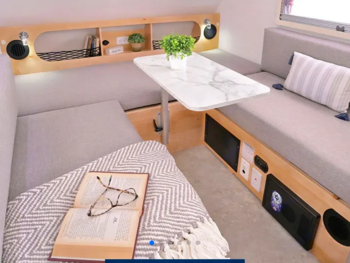 Cozy RV rental interior featuring a bright dinette with gray cushioned seating, a marble-look table, and built-in storage.. nuCamp T@B 2026
