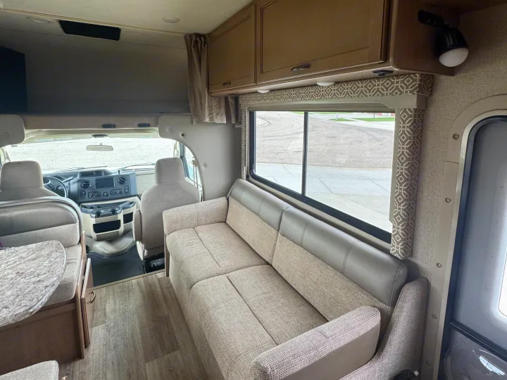 Bright and inviting RV rental interior showcasing a spacious sofa, large window, overhead storage, and front cockpit.. Thor Freedom Elite 2017