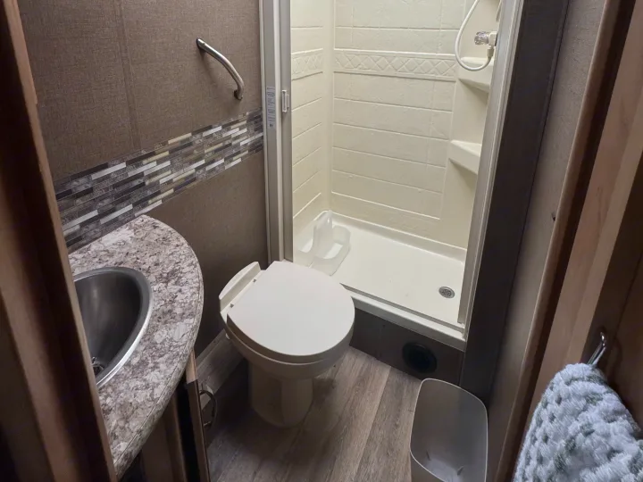 Compact RV rental bathroom with shower, toilet, sink, grab bar, and mosaic tile accent.. Thor Freedom Elite 2017