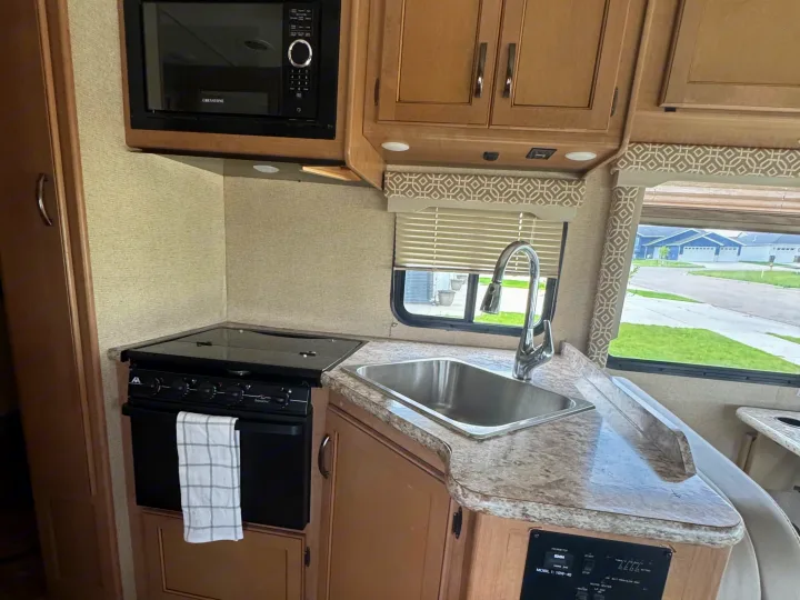 A compact RV rental kitchen featuring a microwave, stovetop, sink, and counter space for preparing meals on the road.. Thor Freedom Elite 2017