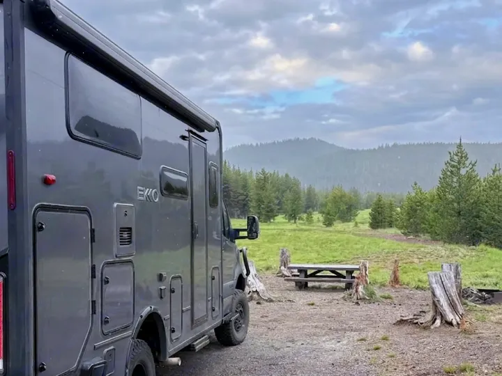 Grey EKKO rv rental parked at a tranquil mountain campsite with a picnic table, surrounded by a lush forest.. Winnebago Ekko 2025