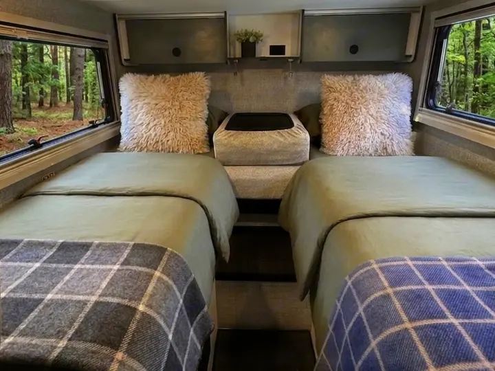 Cozy RV rental interior with two single beds, fluffy pillows, and forest views from large windows.. Winnebago Ekko 2025
