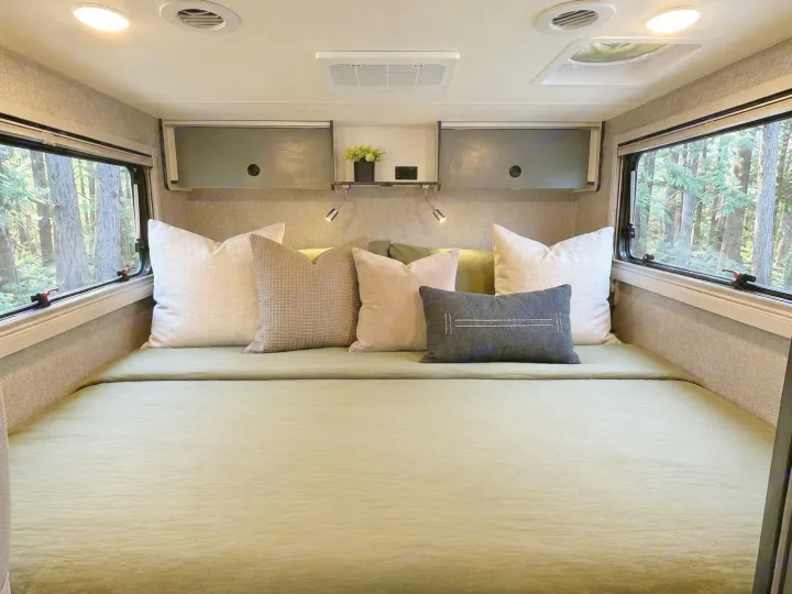 Spacious RV rental bedroom showcasing a bed with green bedding, cozy pillows, and clear forest views from large windows.. Winnebago Ekko 2025