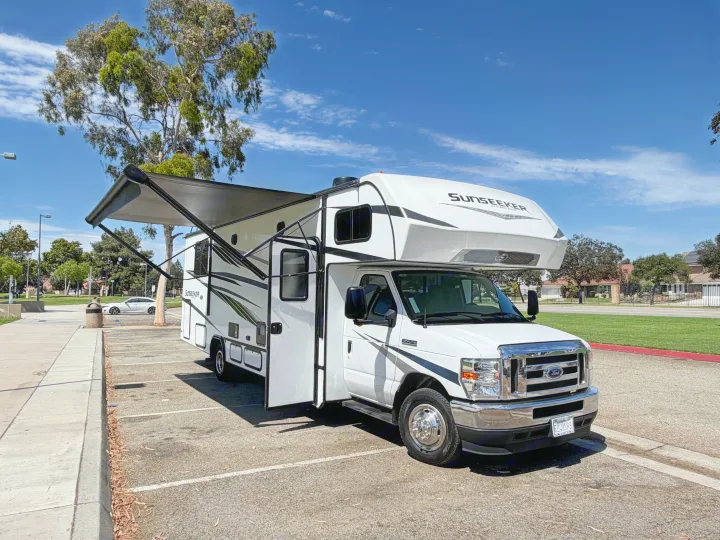 This white Sunseeker RV rental is parked with its awning extended and doors open on a sunny day, ready for an outdoor adventure.. Forest River Sunseeker LE 2024