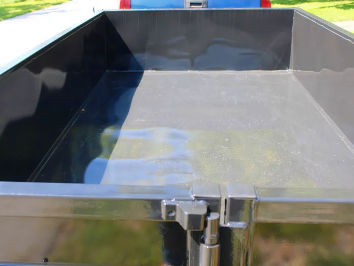 Empty, clean cargo bed of a utility trailer or truck, ready for your RV rental hauling needs. Reflective dark metal surface.. Big Tex 70SR 2027