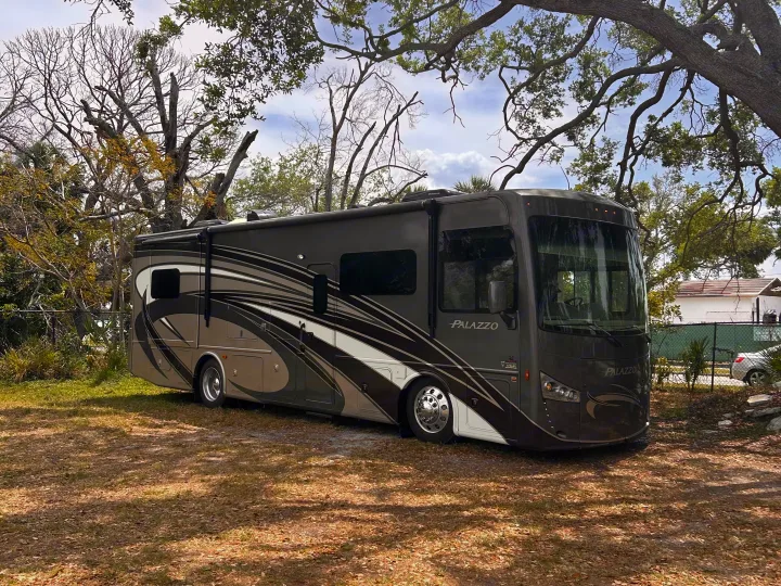 This Palazzo RV rental, a large motorhome, is parked under trees, ready for an outdoor travel adventure.. Thor Palazzo 2016