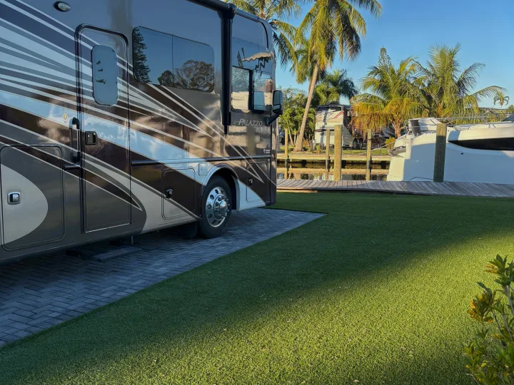 Palazzo RV rental parked on a paved site by a sunny waterfront. Boats and palm trees complete this tropical escape.. Thor Palazzo 2016