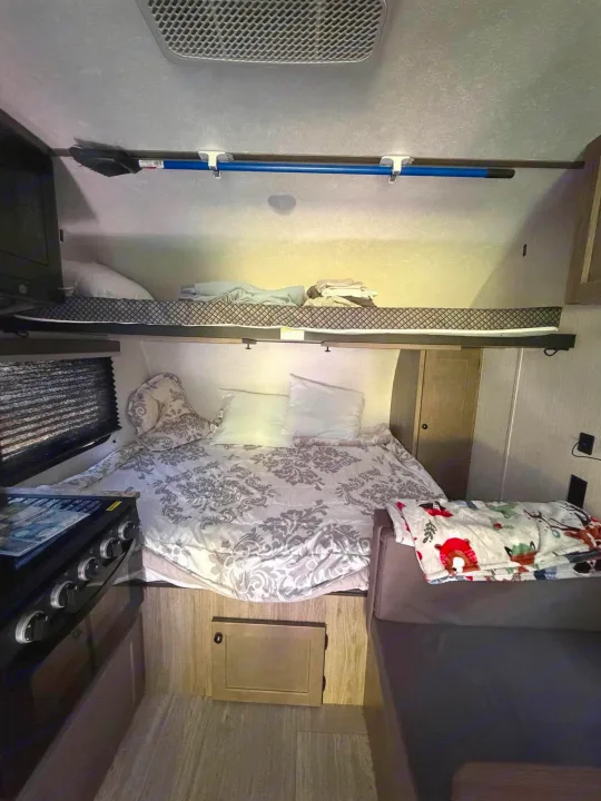 RV rental interior showcasing a comfortable main bed, upper bunk bed, kitchen area with stove, and sofa seating.. Sunset Park RV Sun Lite 2025