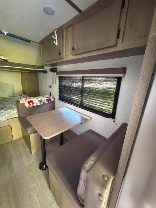 Cozy rv rental interior with a dinette, bunk bed, and overhead cabinets, perfect for travel accommodations.. Sunset Park RV Sun Lite 2025