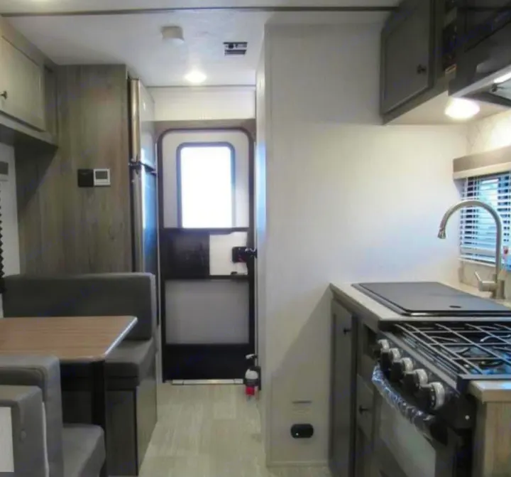Explore your next rv rental: a cozy interior featuring kitchen appliances, a dining booth, and an entry door.. Sunset Park RV Sun Lite 2025
