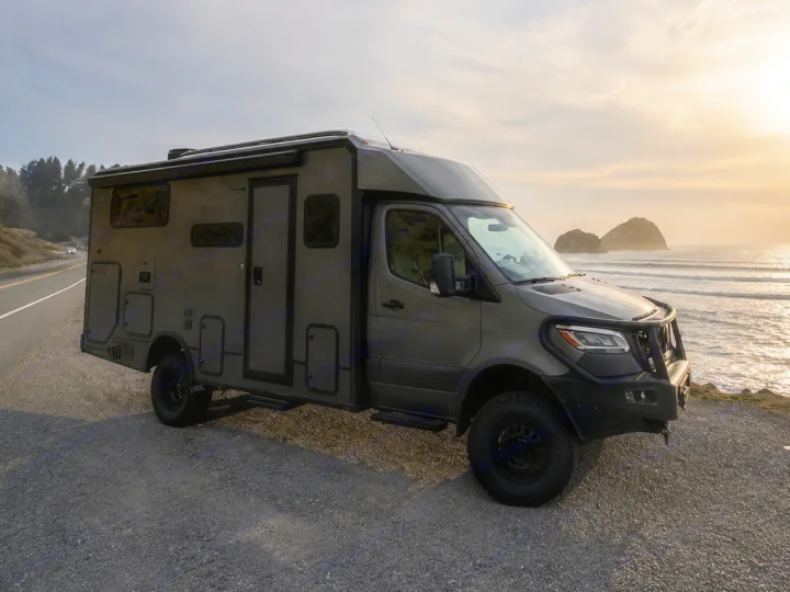 This rugged rv rental, an off-road camper van, is parked overlooking a beautiful ocean sunset with sea stacks.. Winnebago Ekko 2025