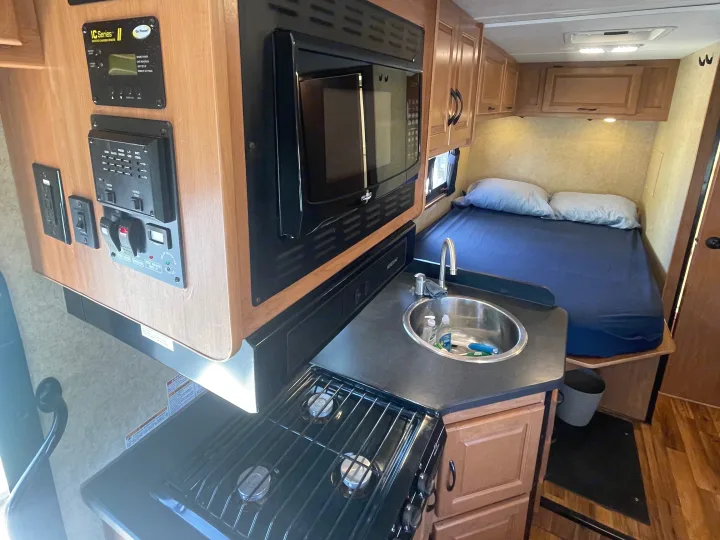 RV rental interior: a compact kitchen with a stove, sink, microwave, and a cozy bedroom area.. Thor Majestic 2017