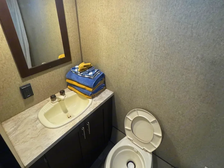 This RV rental bathroom includes a small sink, mirror, wall outlet, dark vanity, toilet with open lid, and folded towels.. Forest River Cherokee Wolf Pup 2016