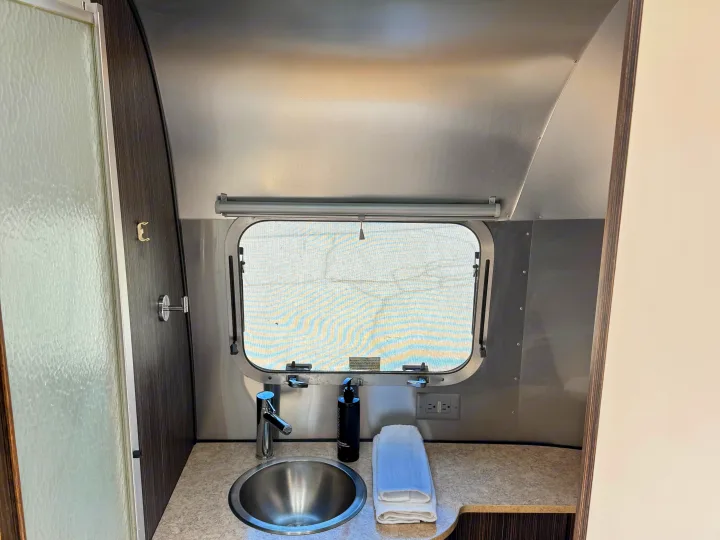 RV rental interior: A compact bathroom vanity with a stainless steel sink, faucet, towels, and a frosted shower door.. Airstream International 2017