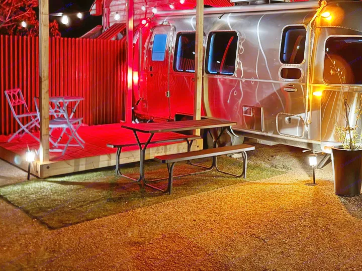 Experience this stylish Airstream RV rental at night, with a red-lit deck and cozy orange-lit picnic area for glamping.. Airstream International 2017