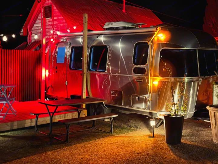 Experience a unique RV rental: a stylish Airstream, bathed in warm red light, set up as cozy outdoor accommodation with a picnic table.. Airstream International 2017
