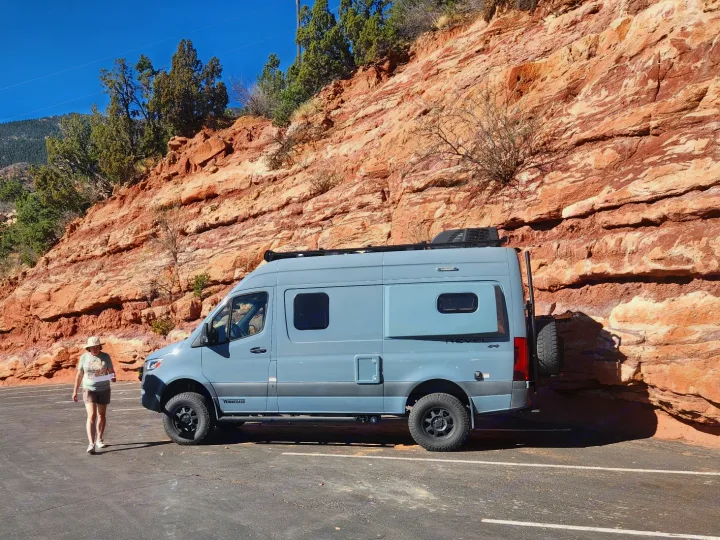 A person walks near a Winnebago Revel camper van, an ideal RV rental for exploring scenic red rock country.. Winnebago Revel 2021