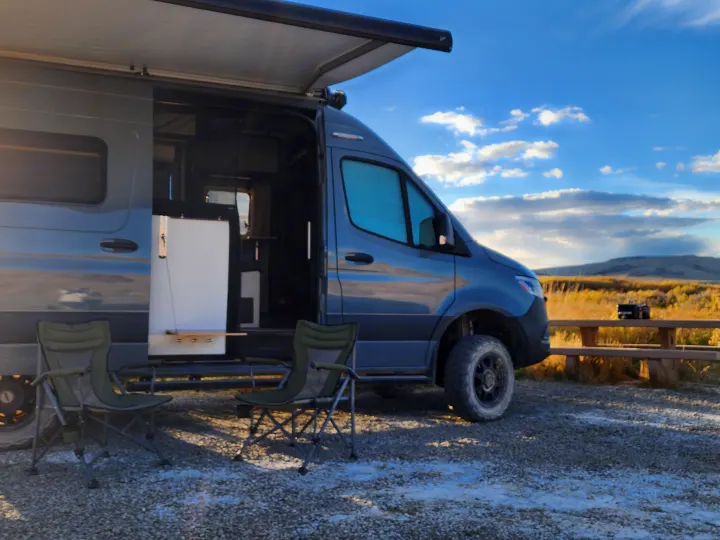 Experience van life with this cozy grey rv rental camper van, side door open, awning extended, chairs set up for outdoor relaxation.. Winnebago Revel 2021