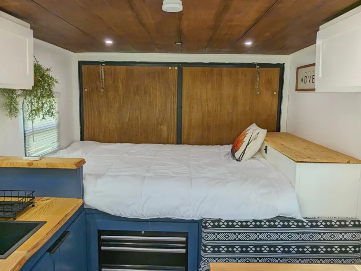 Inside a cozy RV rental: a spacious bed, a modern kitchen with blue cabinets, and a dining nook.. Diamond Cargo 16x8.5 2023