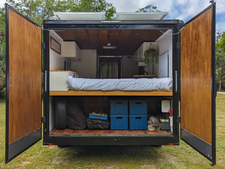 Converted cargo trailer rv rental with rear doors open, revealing a cozy bed, ample storage, and solar panels.. Diamond Cargo 16x8.5 2023