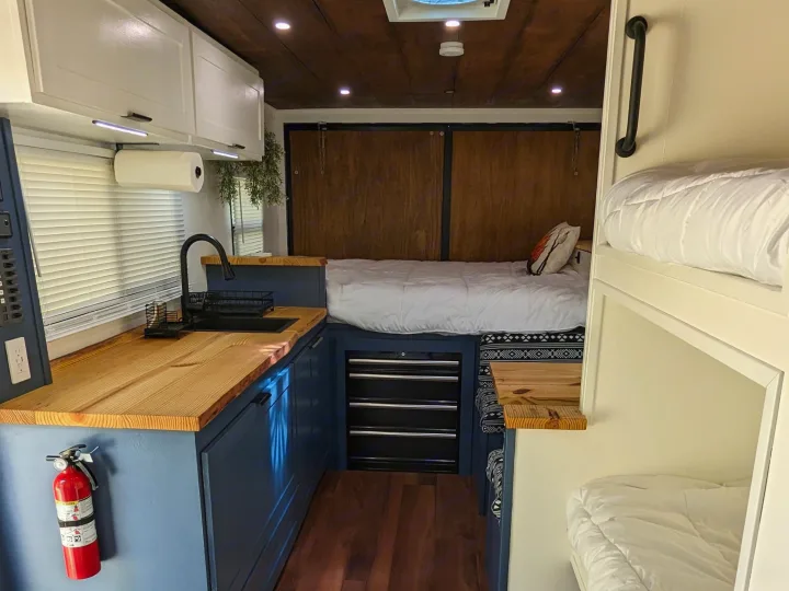 RV rental: Cozy camper van interior with a full kitchen, bed, and bunk beds, featuring a wooden ceiling.. Diamond Cargo 16x8.5 2023