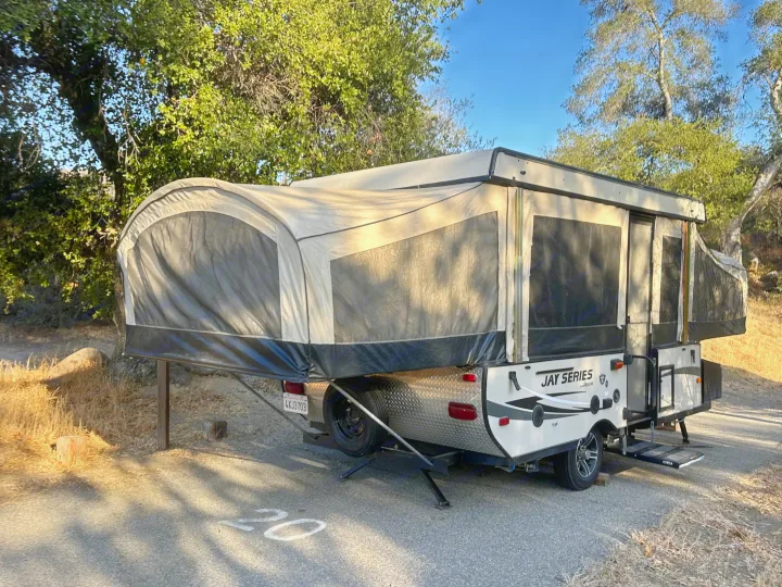 This RV rental, a Jayco pop-up camper, is fully set up at a shaded campsite, ready for adventure in nature.. Jayco 1209SC 2016