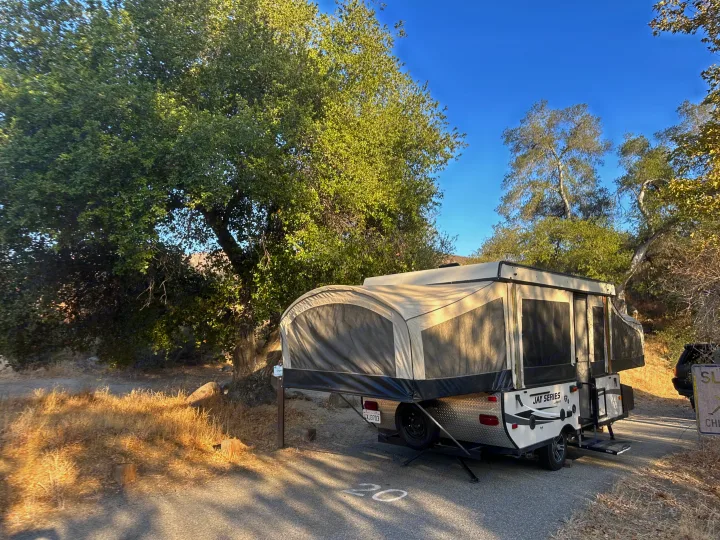 A Jayco pop-up rv rental is fully set up at a sunny, scenic campsite. Ready for outdoor adventure amidst trees.. Jayco 1209SC 2016