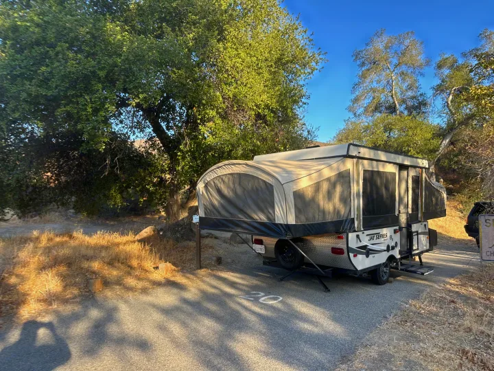 An RV rental pop-up camper is set up at campsite 20, nestled among green trees, ready for a camping trip.. Jayco 1209SC 2016