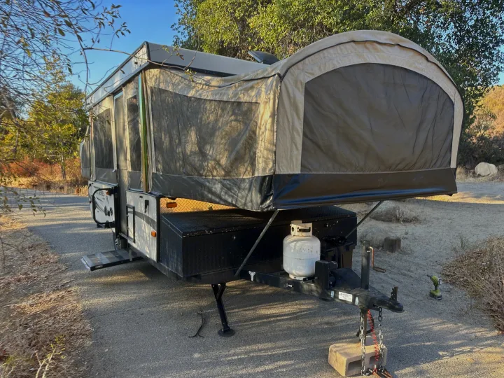 This pop-up camper RV rental is fully set up at a rustic campsite, ideal for outdoor adventures and camping trips.. Jayco 1209SC 2016