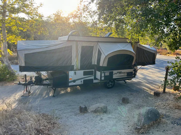 This pop-up camper for your next RV rental is parked at a sunny campsite, ready for adventure.. Jayco 1209SC 2016