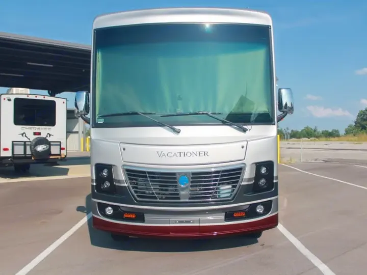 Front view of a silver Class A motorhome rental, a Vacationer, with a white Cherokee travel trailer parked behind it.. Holiday Rambler Vacationer 2022