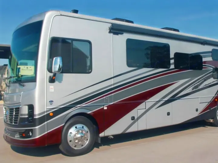 Modern Class A RV rental featuring a silver exterior with striking maroon and grey stripes, parked outdoors under a clear sky.. Holiday Rambler Vacationer 2022