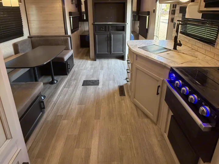 Inside this modern RV rental: a kitchen with stove, sink, dining booth, and light wood-look flooring, offering comfort for travel.. Jayco Jay Flight SLX Rocky Mountain Edition 2022