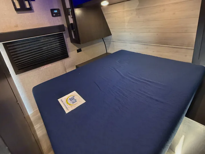 RV rental bedroom: a blue Serta mattress, window with blinds, and control panel on a light wood-paneled wall.. Jayco Jay Flight SLX Rocky Mountain Edition 2022