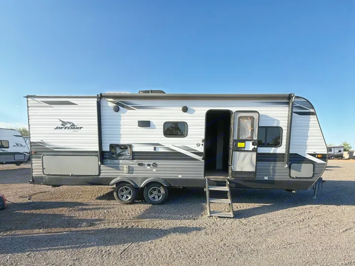 A Jay Flight travel trailer, ideal for rv rental, with its entry door open and steps extended, parked on gravel under a clear sky.. Jayco Jay Flight SLX Rocky Mountain Edition 2022