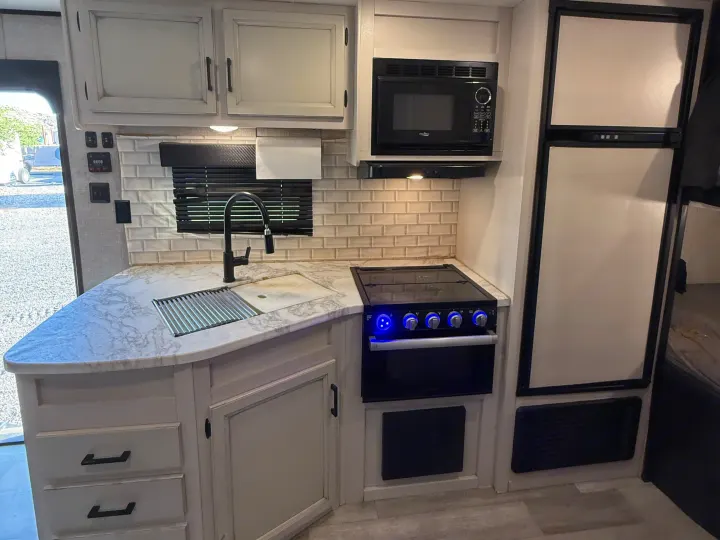 Well-equipped RV rental kitchen featuring a sink, microwave, oven, and refrigerator for comfortable travels.. Jayco Jay Flight SLX Rocky Mountain Edition 2022