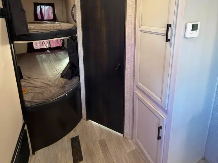 An rv rental interior: bunk beds on left, dark door, light cabinets with a wall thermostat on the right.. Jayco Jay Flight SLX Rocky Mountain Edition 2022