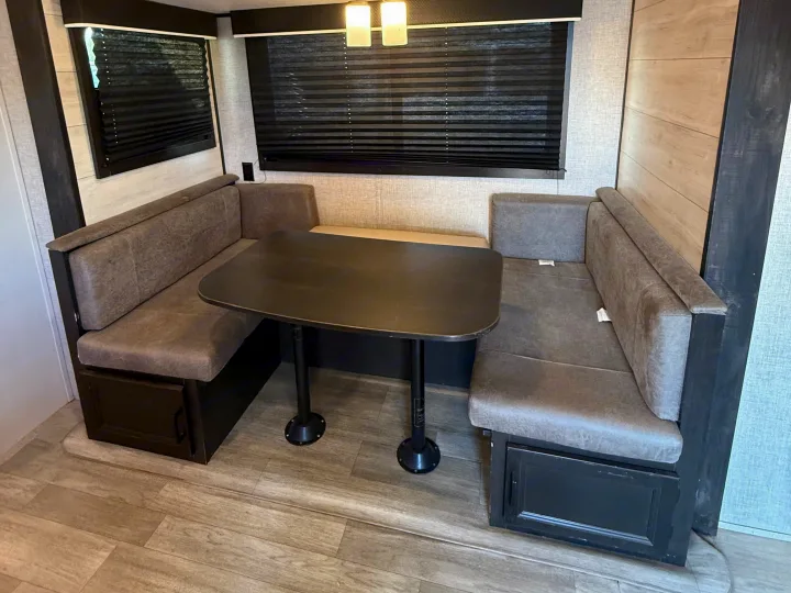 This rv rental features a cozy U-shaped dinette with grey benches, a dark table, and black window blinds.. Jayco Jay Flight SLX Rocky Mountain Edition 2022
