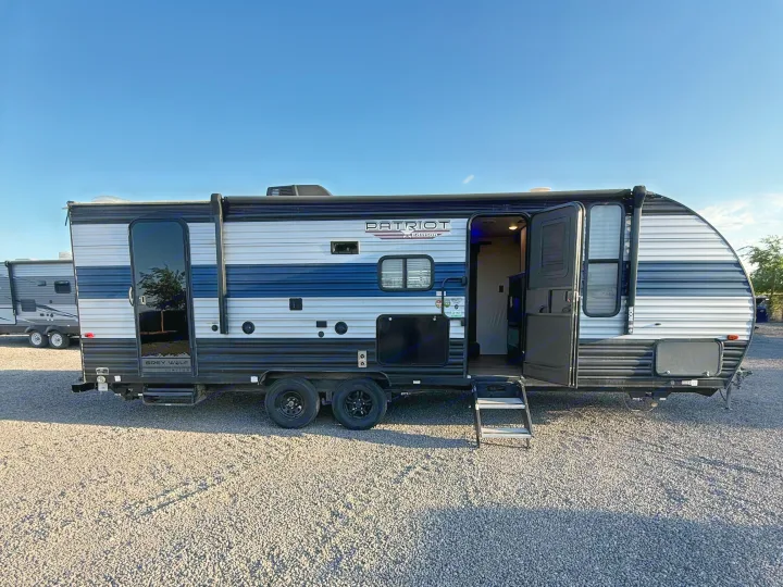 This modern Patriot Edition RV rental, a grey and blue travel trailer, stands ready for adventure with its entry door open.. Forest River Cherokee Grey Wolf 2021