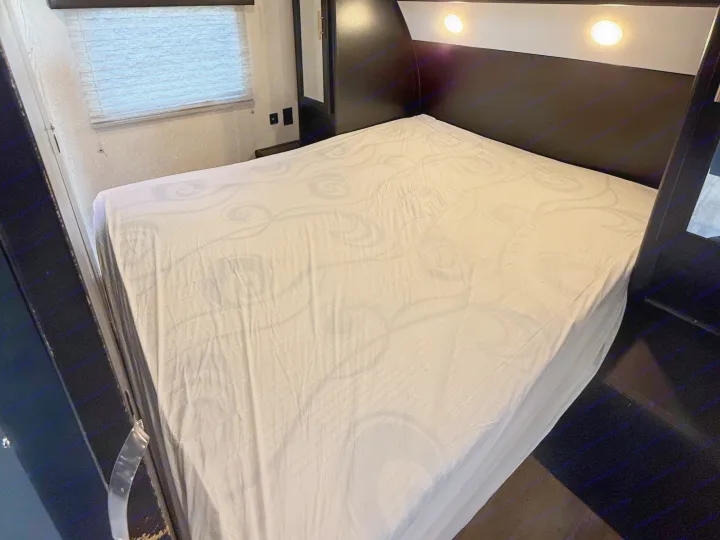 Clean and inviting bed with white patterned sheets in an RV rental, featuring a window and overhead lights.. Forest River Cherokee Grey Wolf 2021